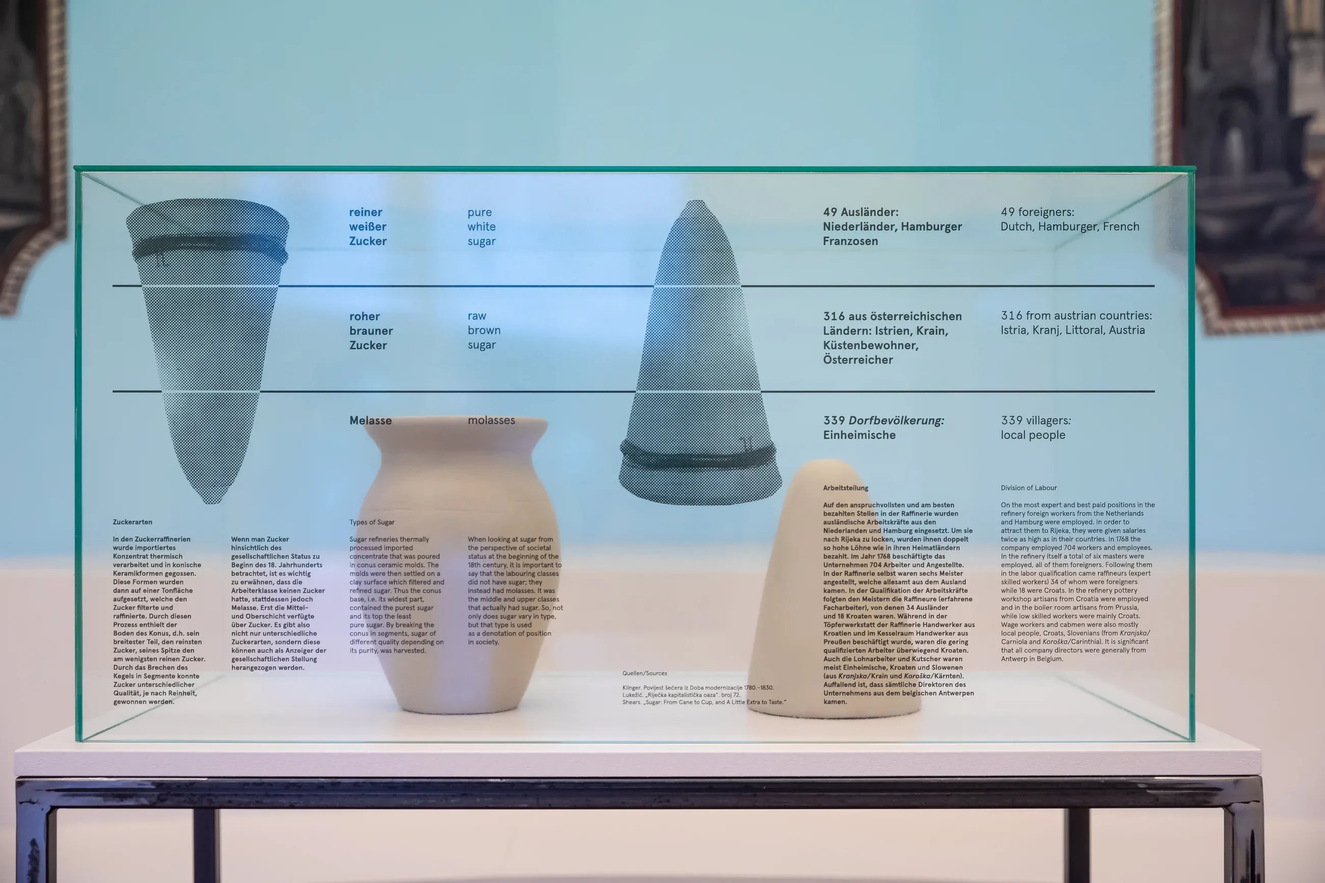 A vitrine with ceramic sugar moulds and jars, with printed labels on the glass
