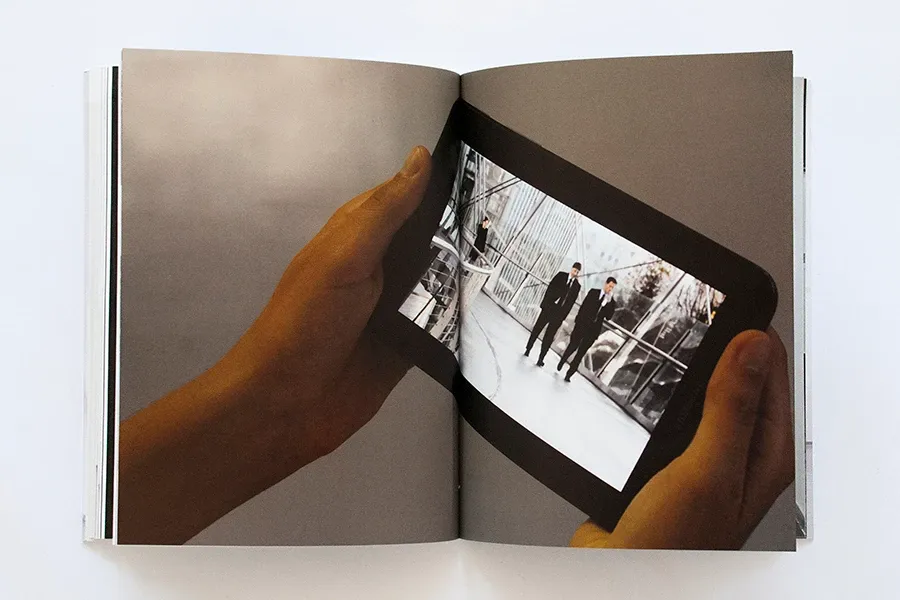 A full-spread photograph of hands holding a tablet that shows a black-and-white street photograph