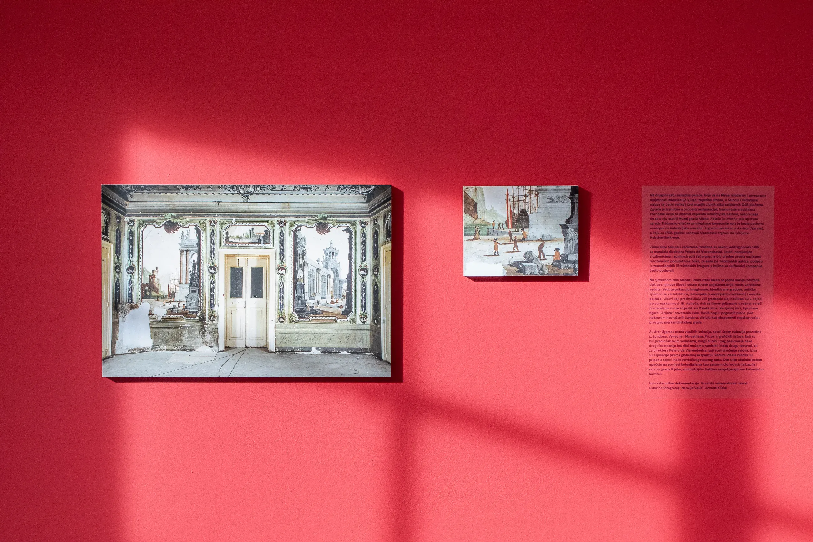 Two framed photographs of the wall paintings and a text panel on the red wall