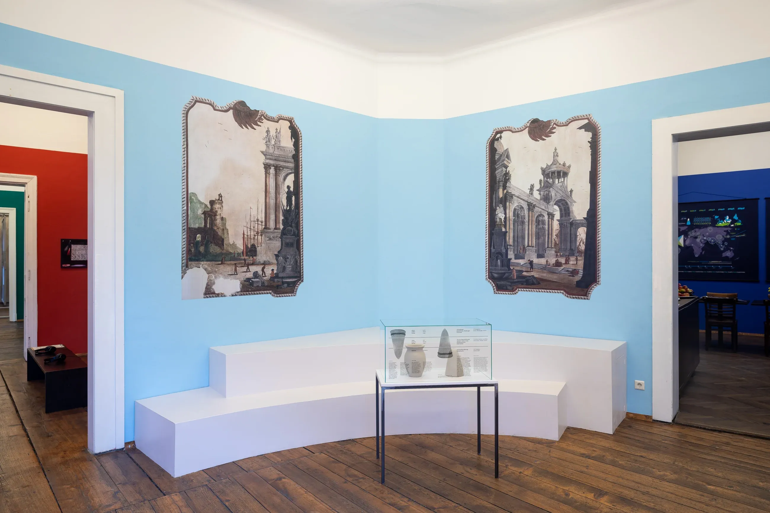 A blue room with two prints of the vedute, a curved white bench and a vitrine